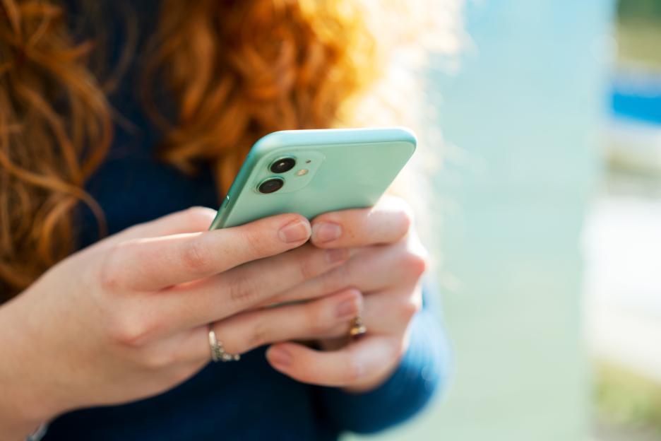 A young woman with curly red hair holding a mint green smartphone.