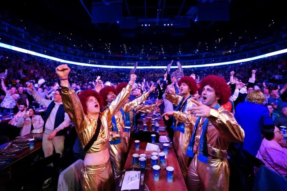 Fans wearing gold outfits and red afros celebrate in the stands at the BetMGM Premier League Play-Offs.
