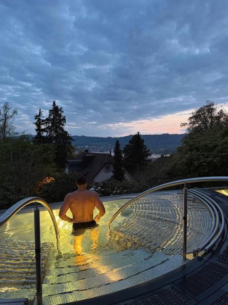 Tommy Fury in a hot tub overlooking a Swiss landscape at dusk.