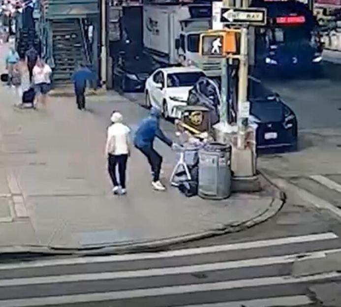 A person in blue attempts to steal a package from a delivery cart on a city street.
