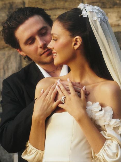 Brooklyn Beckham embracing Nicola Peltz, who is wearing a white wedding dress and veil.