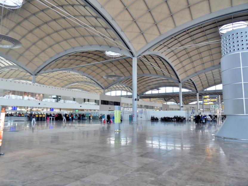 Interior of Alicante-Elche Miguel Hernández Airport, showing people and a curved roof structure.