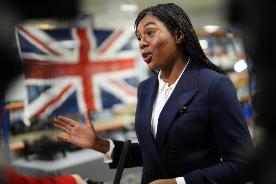 Kemi Badenoch speaks to an audience with a blurred Union Jack flag in the background.