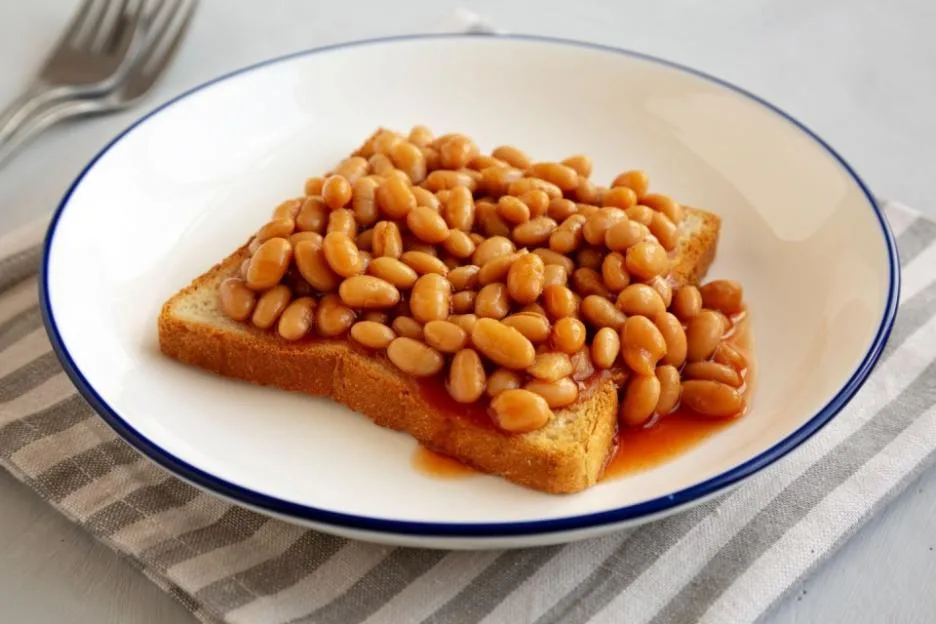 A slice of toast topped with baked beans in tomato sauce on a white plate with a blue rim.