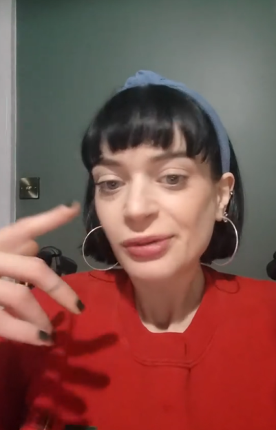 Woman with a blue headband and red shirt holding up two fingers.