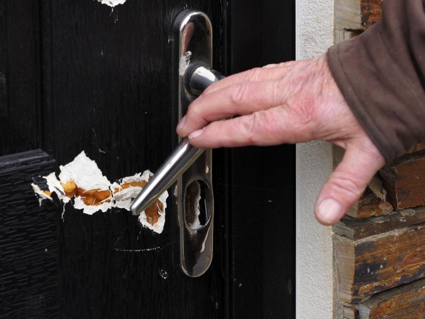 A person's hand opening a metal door handle on a black door with peeled paint.