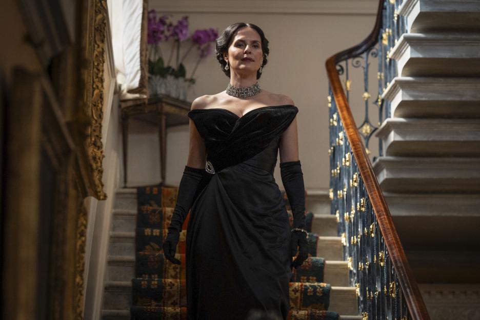 Adele Fairley (Leanne Best) in a black off-the-shoulder gown, walking down a grand staircase.