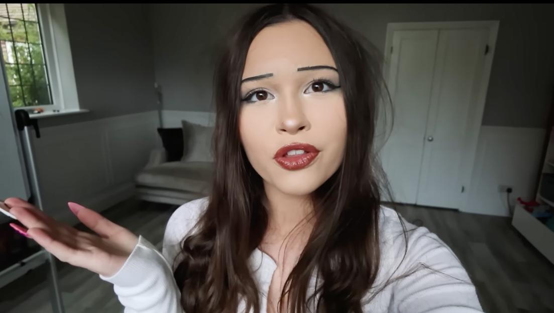 A woman with exaggerated makeup on her face, and a young girl smiling in the background.