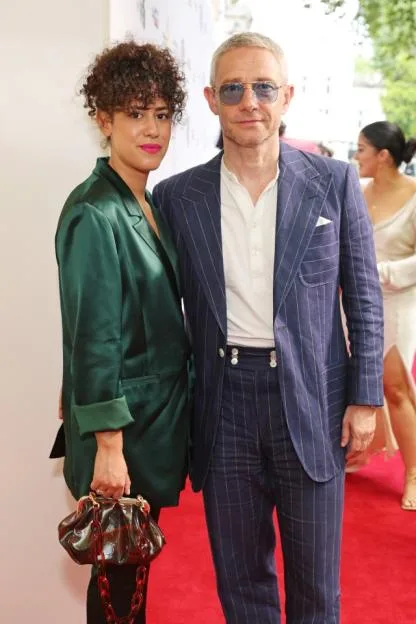 Rachel Mariam in a green satin suit and Martin Freeman in a blue pinstripe suit and sunglasses stand together on a red carpet.