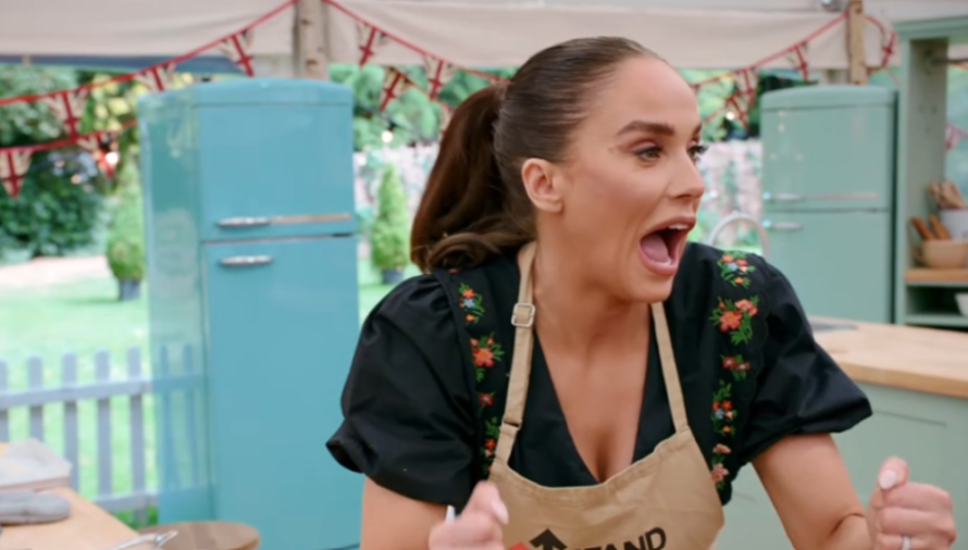 Woman with a ponytail and an apron reacting with an open mouth in a kitchen.