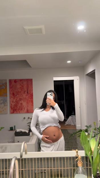 Influencer Mya Mills poses in a mirror, holding her visibly pregnant belly.