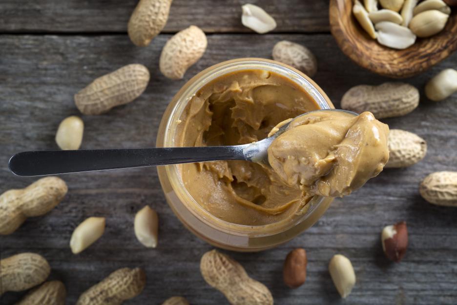 Spoon and pot of peanut butter on wooden background