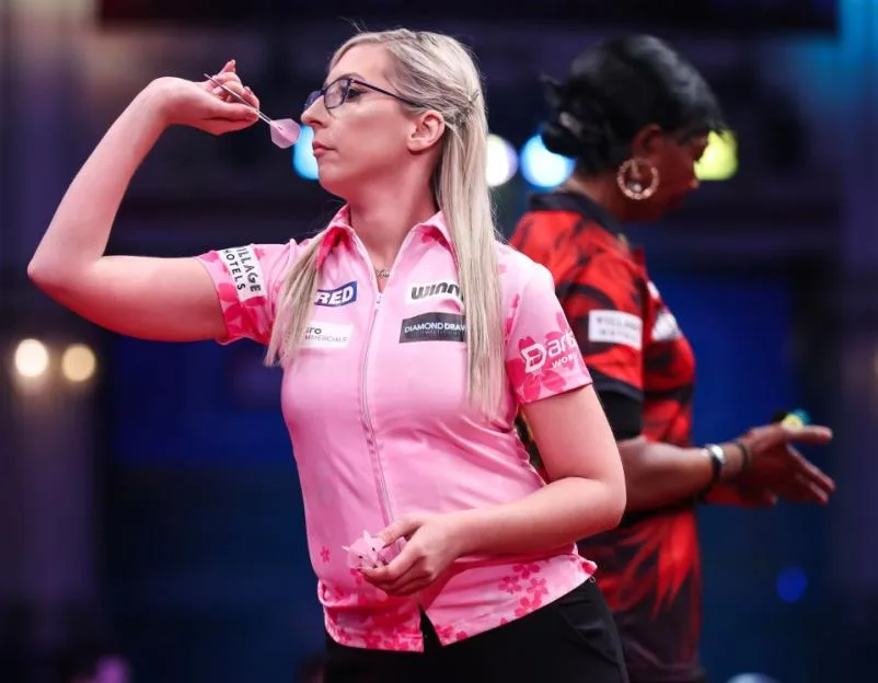 Fallon Sherrock focuses intently as she prepares to throw a dart, holding another in her other hand.