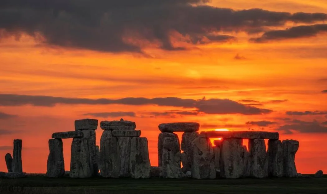 Stonehenge silhouetted against a brilliant orange sunset with dark clouds.