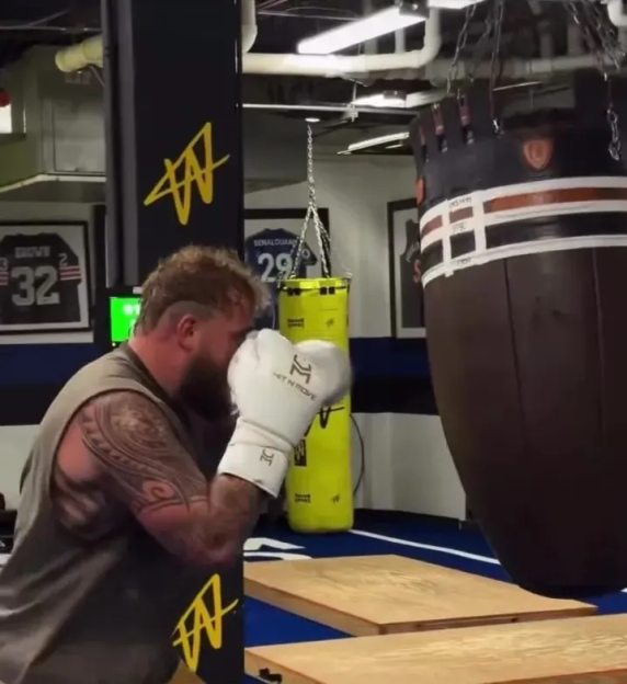 Man in a gym throwing a punch at a hanging punching bag.