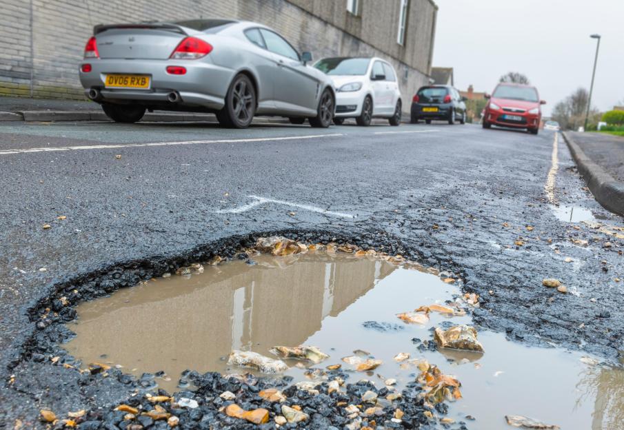Pothole in an asphalt road filled with rain water in England, UK. Damaged road surface. Road in need or repair. Large potholes. Big pothole.