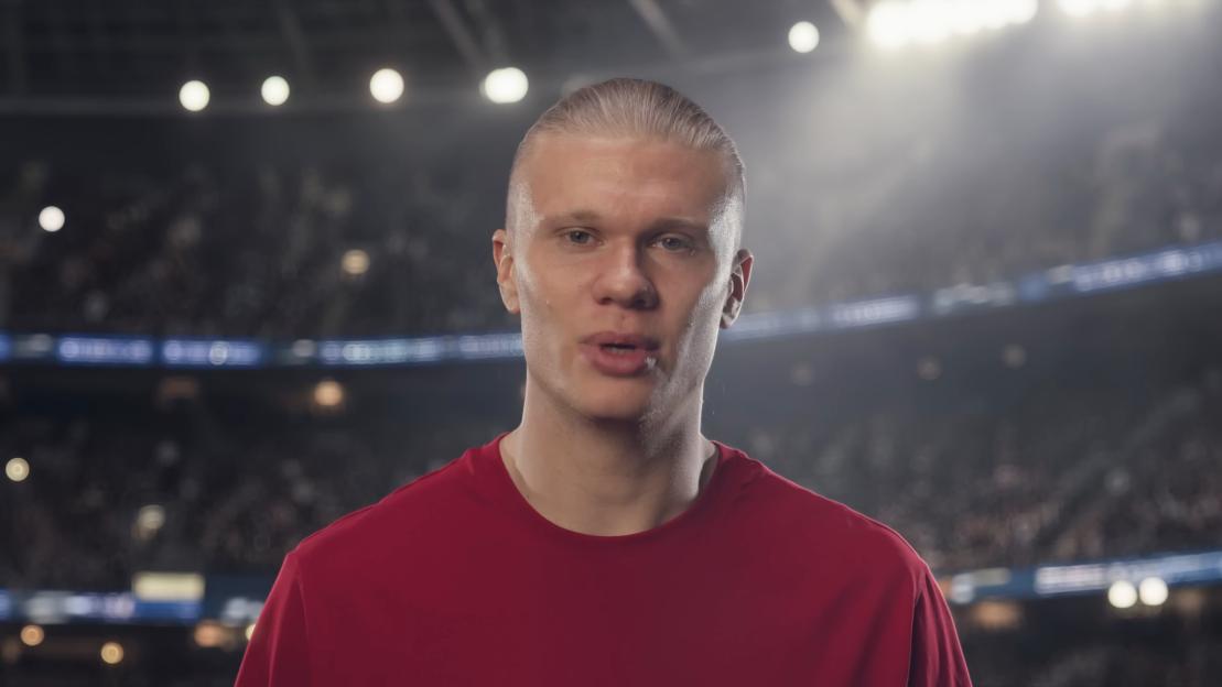 Blonde man in a red shirt with lights from a stadium in the background.