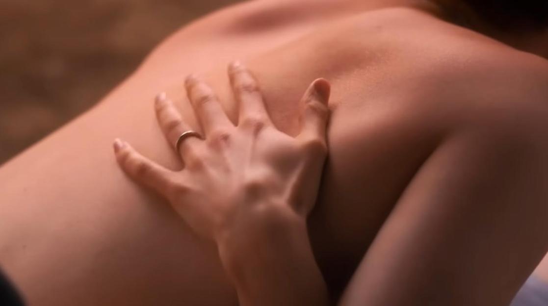 A hand with a ring on the finger caressing a bare back.