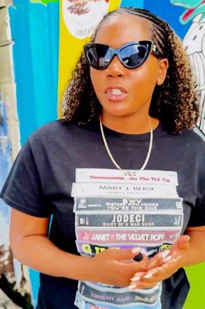 A woman wearing sunglasses and a black t-shirt with a stack of cassette tapes printed on it.