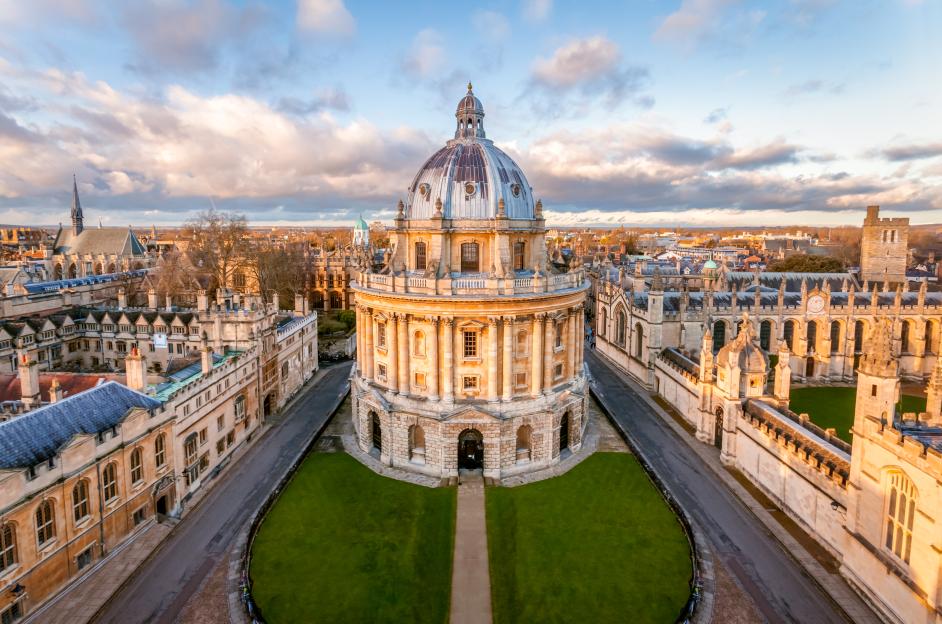 High-angle view of The Radcliffe Camera in Oxford, England, a domed, circular building surrounded by other university architecture under a partially cloudy sky.