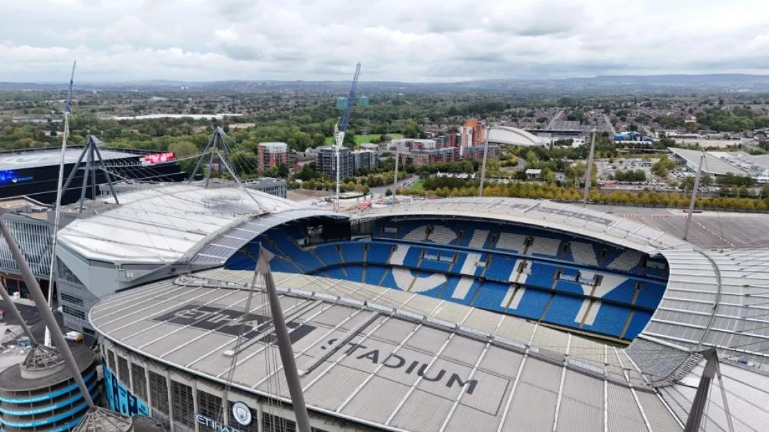 Aerial view of the Etihad Stadium in Manchester, with the word "STADIUM" visible on its roof.