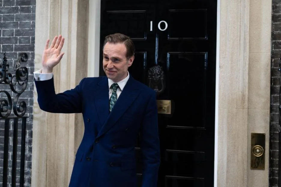 Rafe Spall as Prime Minister Harry Douglas waving in front of the door at 10 Downing Street.