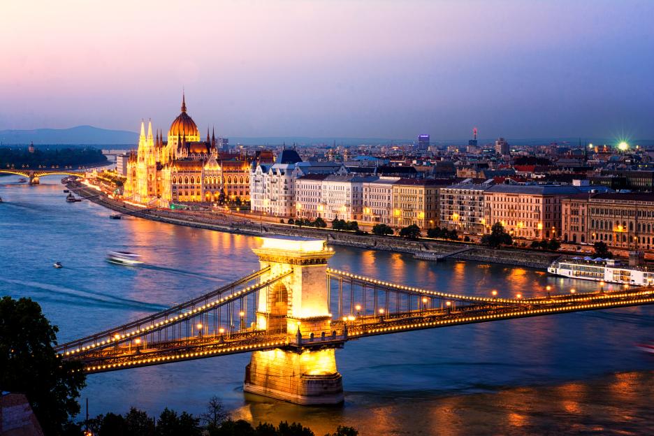 The Hungarian Parliament and the Chain Bridge in Budapest at sunset, with city lights reflecting on the Danube River.