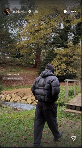 Screen grab of Instagram story showing the back of a person wearing a black puffer jacket and sweatpants, walking near a stream in a wooded area.