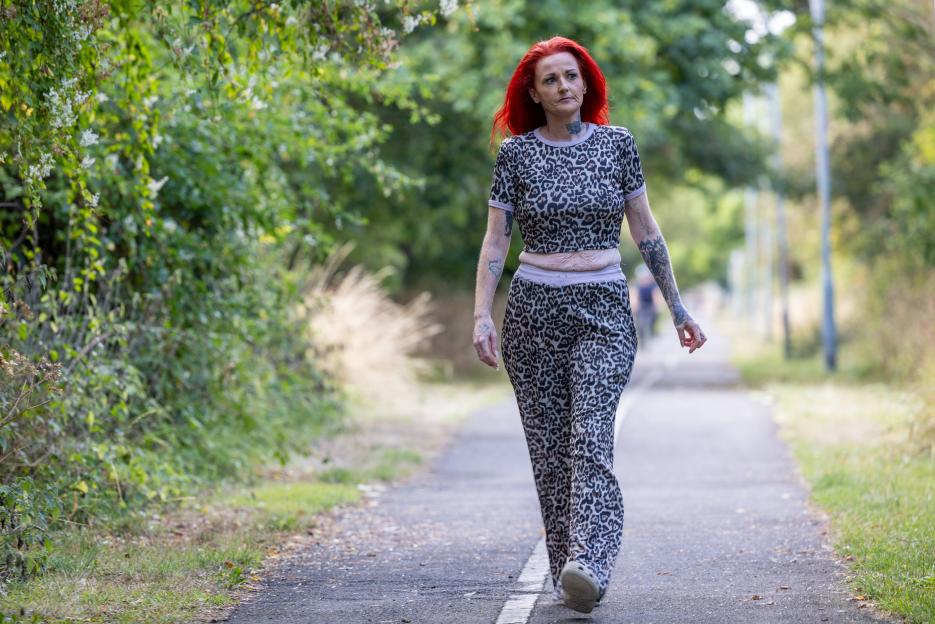 Zoe Johnson, with vibrant red hair, walks outdoors, dressed in a leopard-print top and trousers.