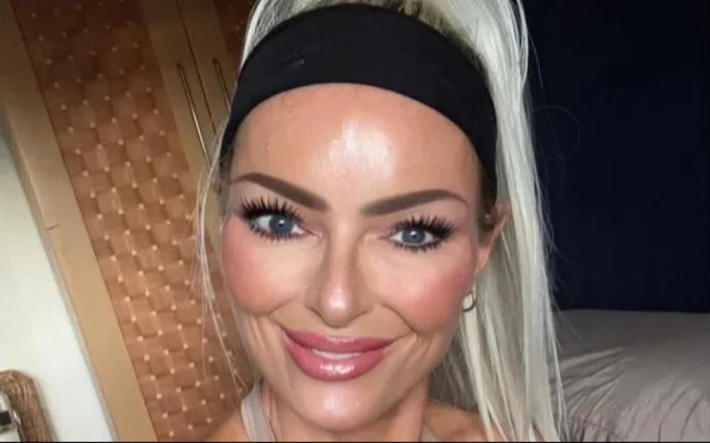 A woman with long blonde hair and blue eyes, wearing a black headband, smiles at the camera.