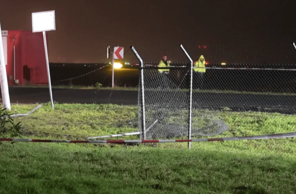 Damaged chain-link fence at Leipzig Airport at night.