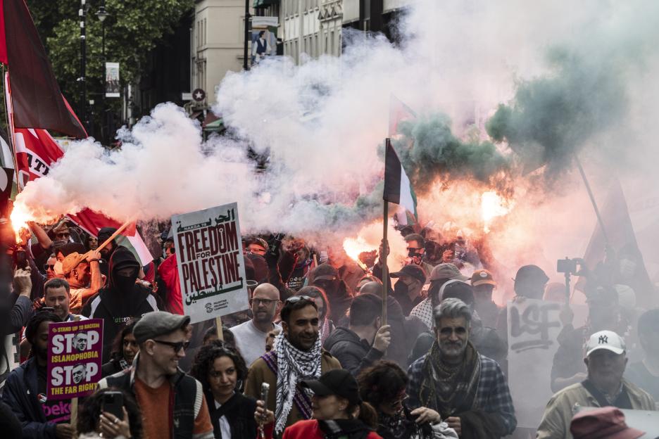Pro-Palestinian marchers with flags and flares filling a street with smoke.
