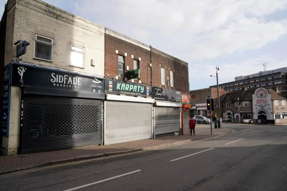 A street view in Dudley showing rows of shops with closed roller shutters along a road with traffic lights.