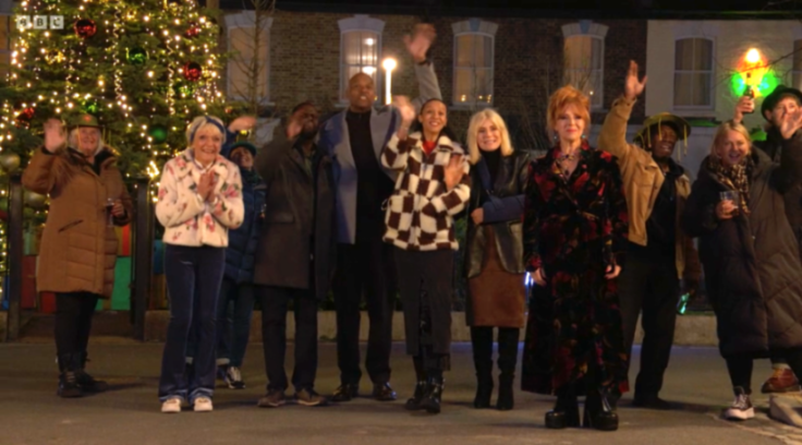 A diverse group of people celebrating at night with a large decorated Christmas tree in the background.
