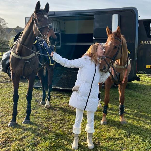 Geri Horner kissing a horse beside another horse.