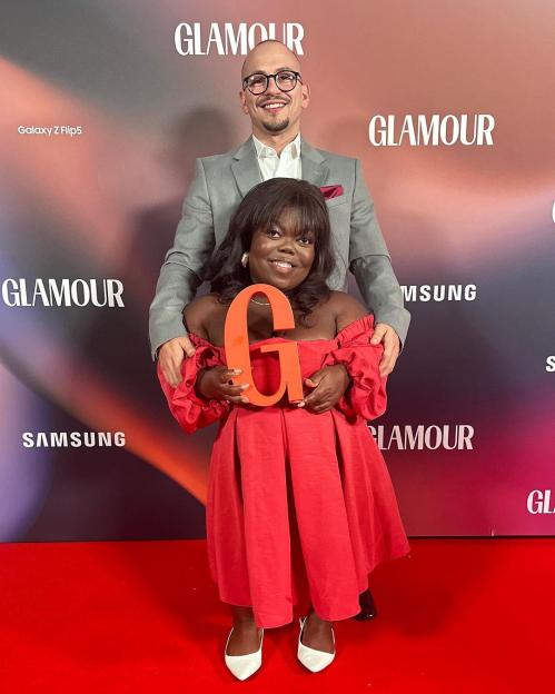 Fats Timbo holding a large orange 'G' award with a man behind her on a red carpet.