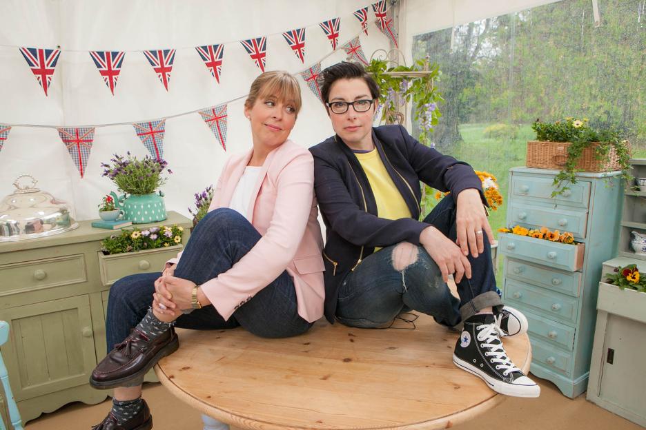 Mel Giedroyc and Sue Perkins sit back-to-back on a round wooden table.