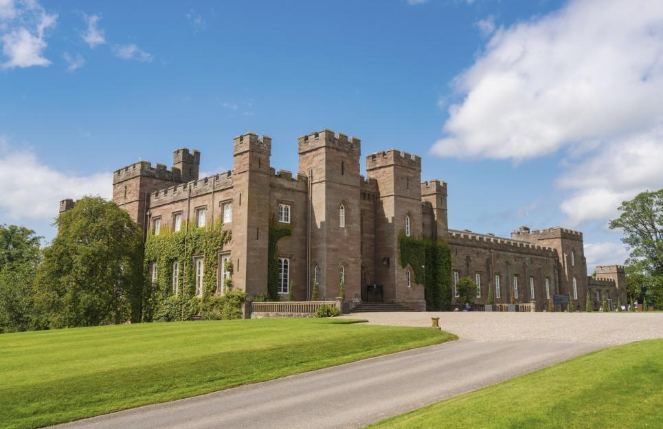 Scone Palace, a large brick building with towers and green ivy climbing its walls, under a blue sky with white clouds.