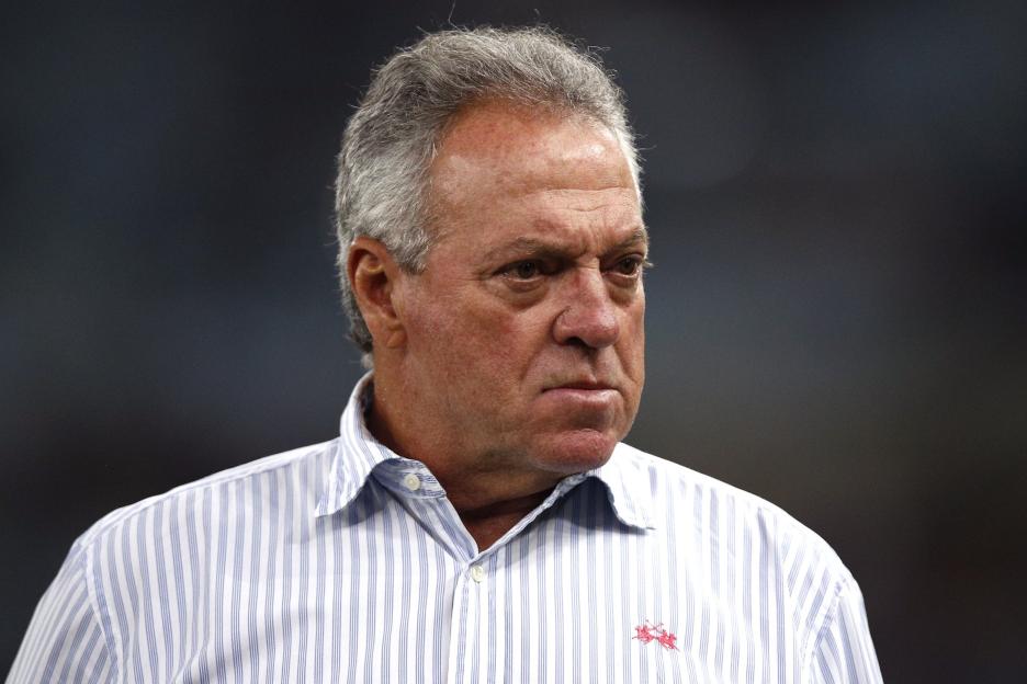 A man with gray hair and a striped shirt with a red horse logo.