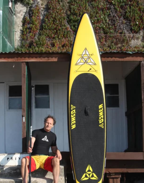 Farrel O’Shea sits next to a yellow and black stand-up paddleboard.
