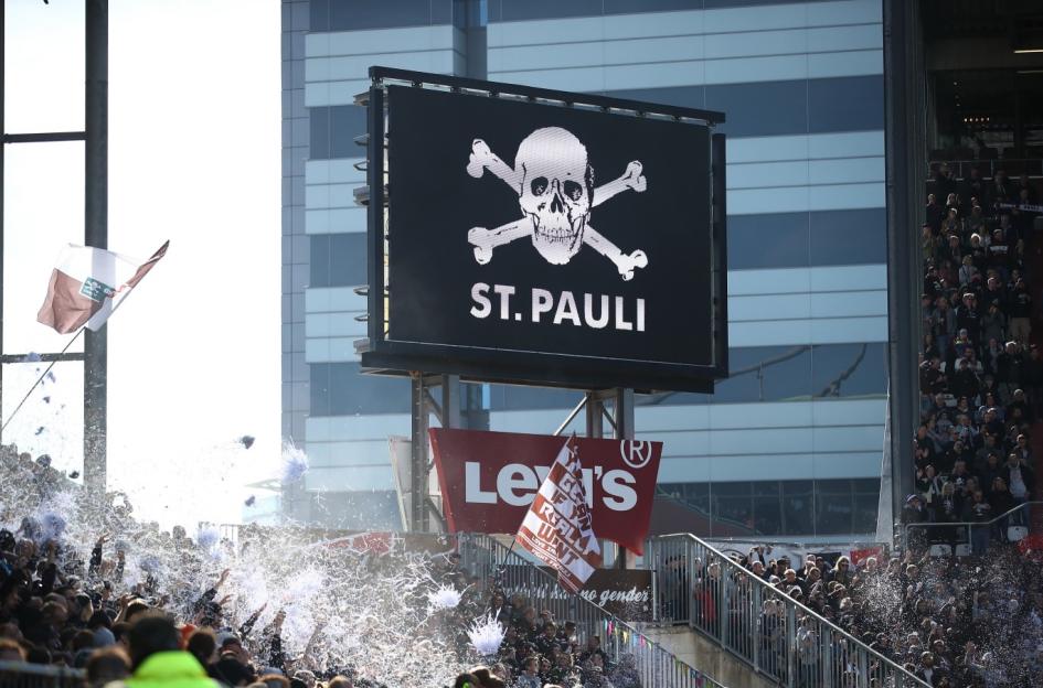 Fans cheering in a stadium with a scoreboard displaying the St. Pauli logo.
