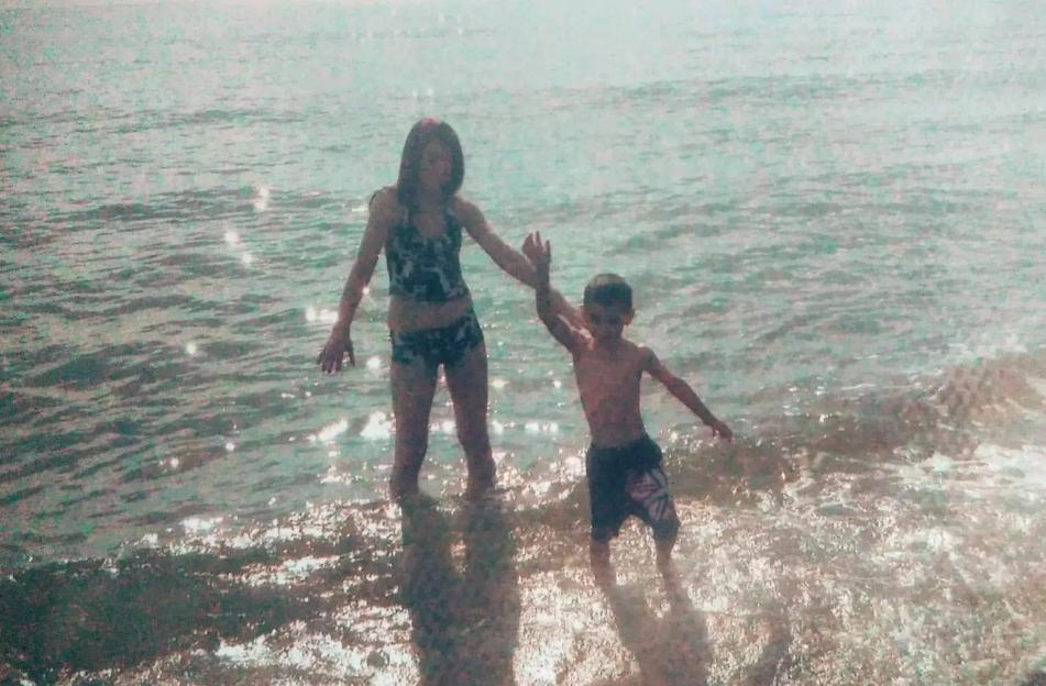 A young boy and girl standing in the ocean, holding hands.