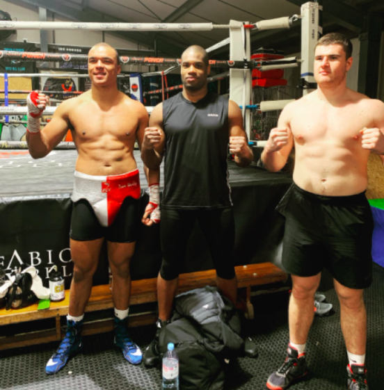 Three boxers standing in a boxing gym, flexing their biceps.