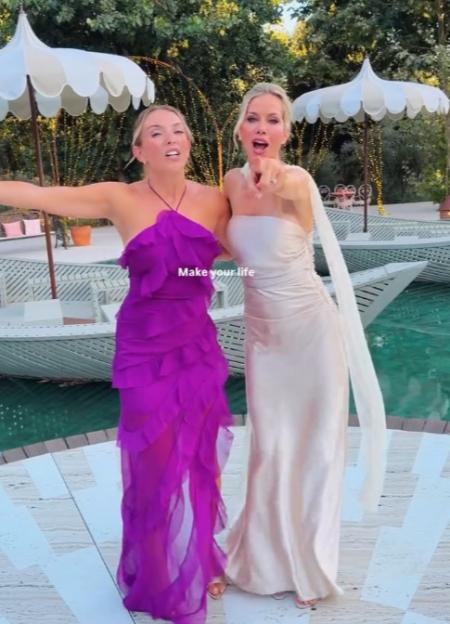 Two women in formal dresses pose by a pool.