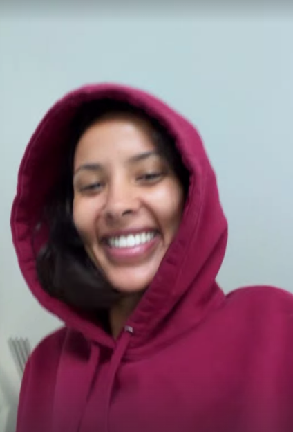 A woman in a maroon hoodie smiling with her teeth showing.