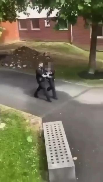 Two police officers restraining a person on a paved area.