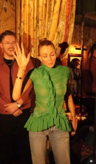 Olivia Attwood posing in a green ruffled top with a man in the background.