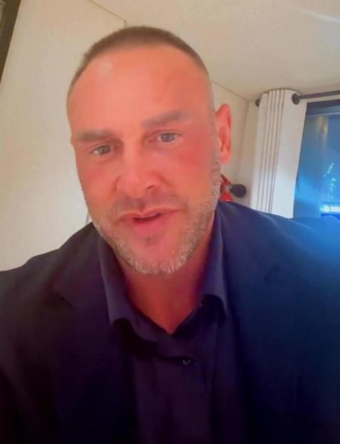 A man with a shaved head and beard, wearing a dark blue shirt, looks directly at the camera.