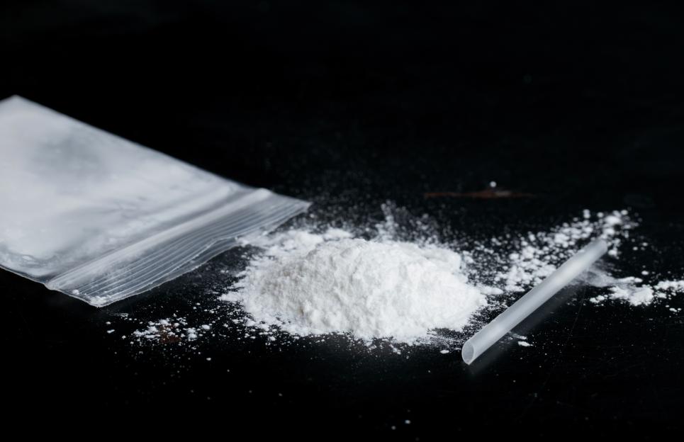 Ketamine drugs and plastic straw on bag of white powder on black wood background.