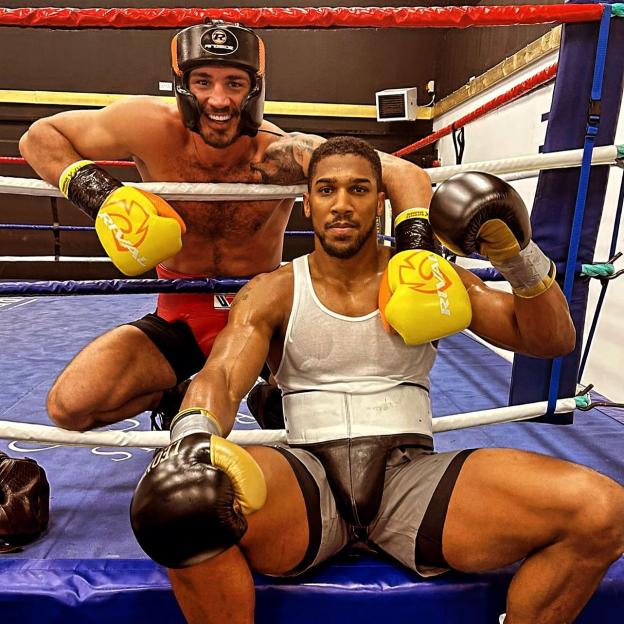 Boxers Argon Smakici and Anthony Joshua pose in a boxing ring.